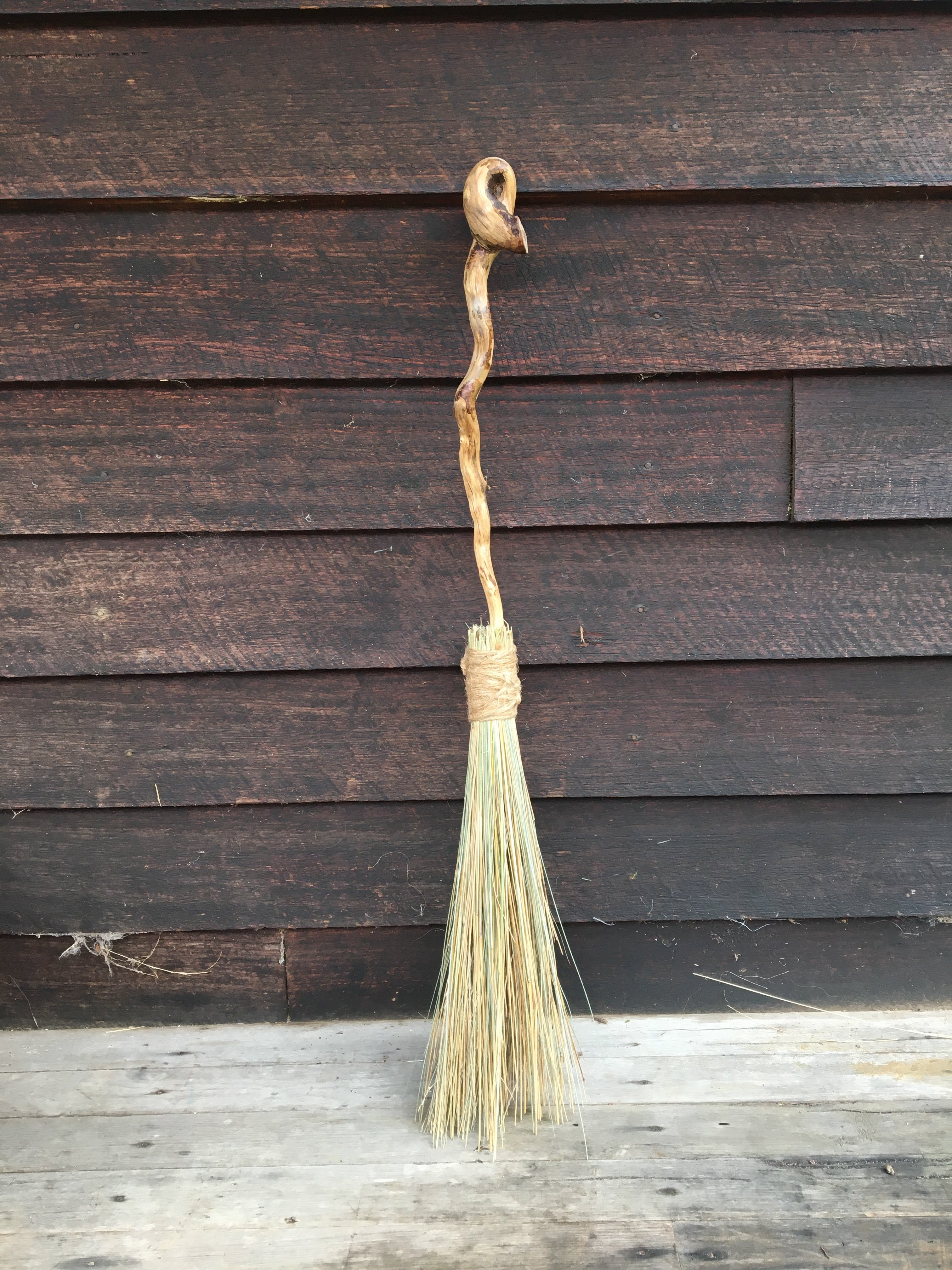 A handmade bush broom with a natural branch handle against dark timber